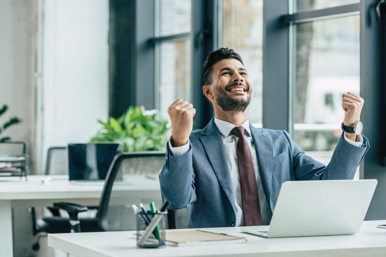 Managed wordpress plans 2 seo, web design & marketing agency town press media Happy businessman looking up and showing winner gesture while sitting at workplace seo, web design & marketing agency town press media